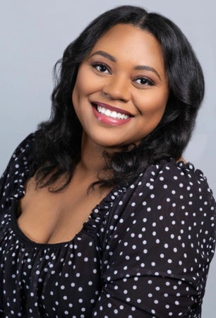 A head-and-shoulders portrait of author Myah Ariel. She is a young Black woman with dark hair and a black and white polka-dot top. She has a warm smile, and her hair is styled in loose waves. The background is a solid gray color.