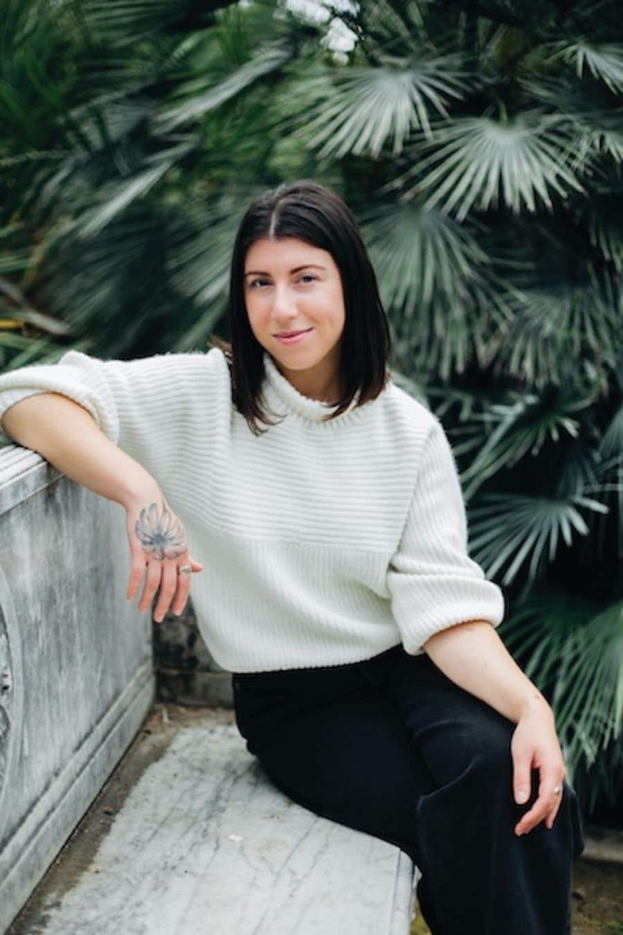 Author photo of Hannah Deitch sitting outside on a cement bench with green florals behind her Author photo of Hannah Deitch sitting outside on a cement bench with green florals behind her