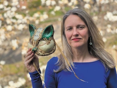 Author photo for Katherine Marsh. Katherine is outside in a purple top and holding out to her right she is holding up a gold masquerade mask of an animal.