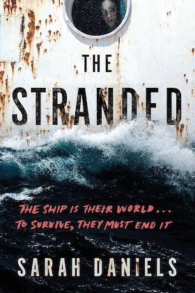 A book cover for "The Stranded" by Sarah Daniels. The cover features a close-up of a weathered, rusty white ship's hull with a round porthole at the top, through which a person's face is partially visible. Below the porthole, the word "THE" is written in small, dark letters above the large, distressed, dark gray title "STRANDED," which appears to be partially submerged in rough, dark blue and white ocean waves depicted below it. Red text in the middle reads, "THE SHIP IS THEIR WORLD... TO SURVIVE, THEY MUST END IT." The author's name, "SARAH DANIELS," is written in large white letters at the bottom, set against the dark ocean. The overall mood is ominous and suggests a survival story at sea.