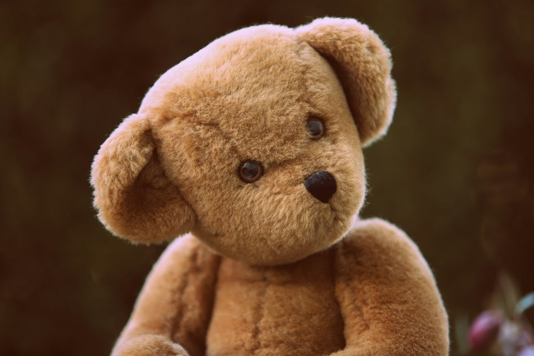 A close up of a tan teddy bear with his head cocked, brown eyes looking off into the distance off-screen.