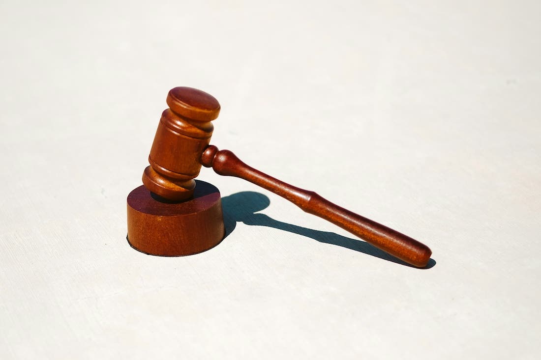 Photo of a wooden judge's gavel resting on a white nondescript backgroun.