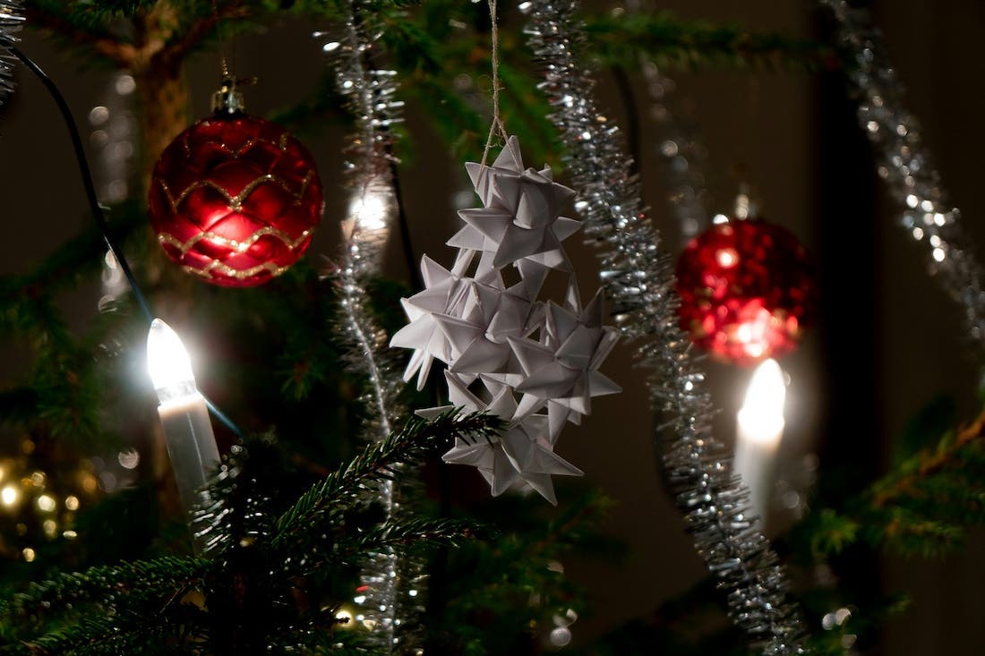 a close up of a yule tree decorated with paper stars and artificial candles