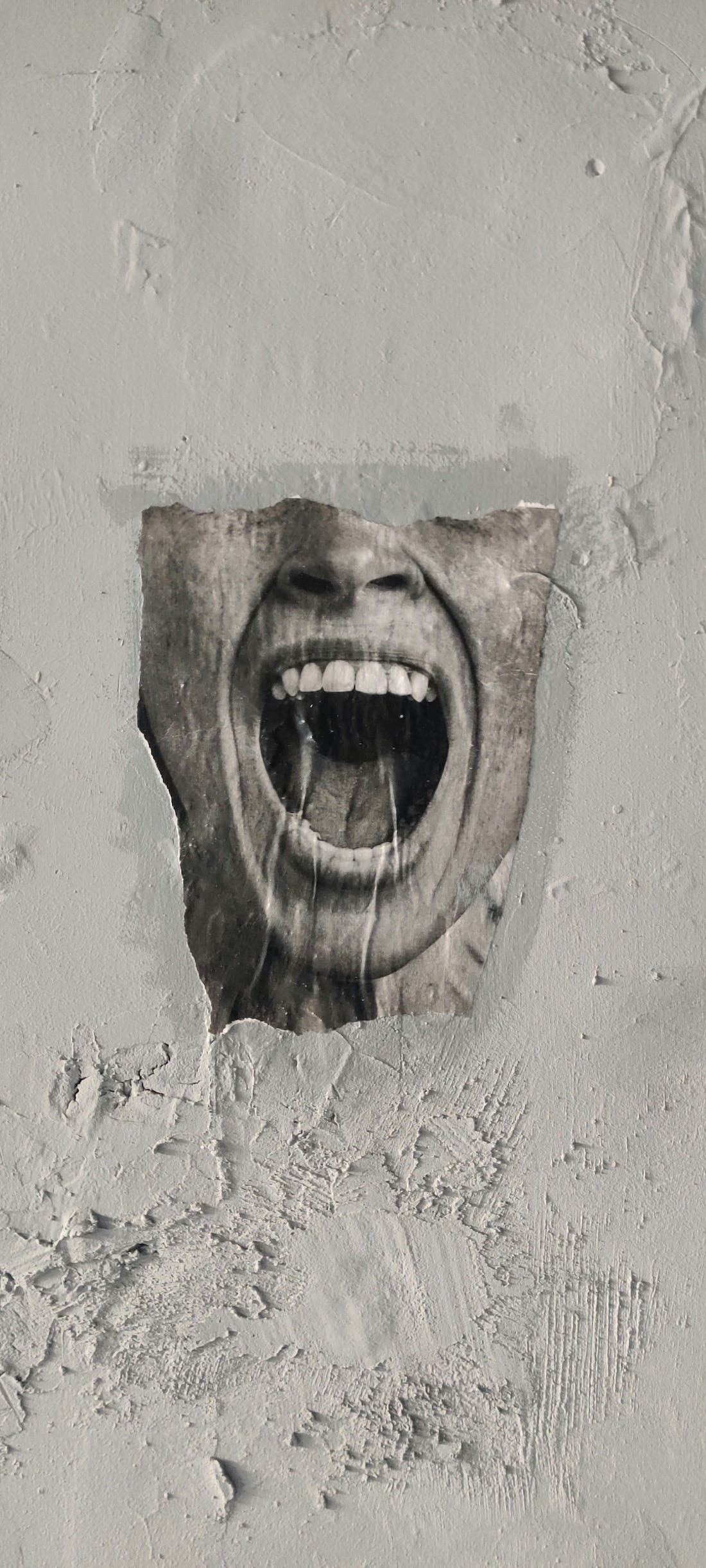An art piece on a concrete wall of a person's mouth open in a scream