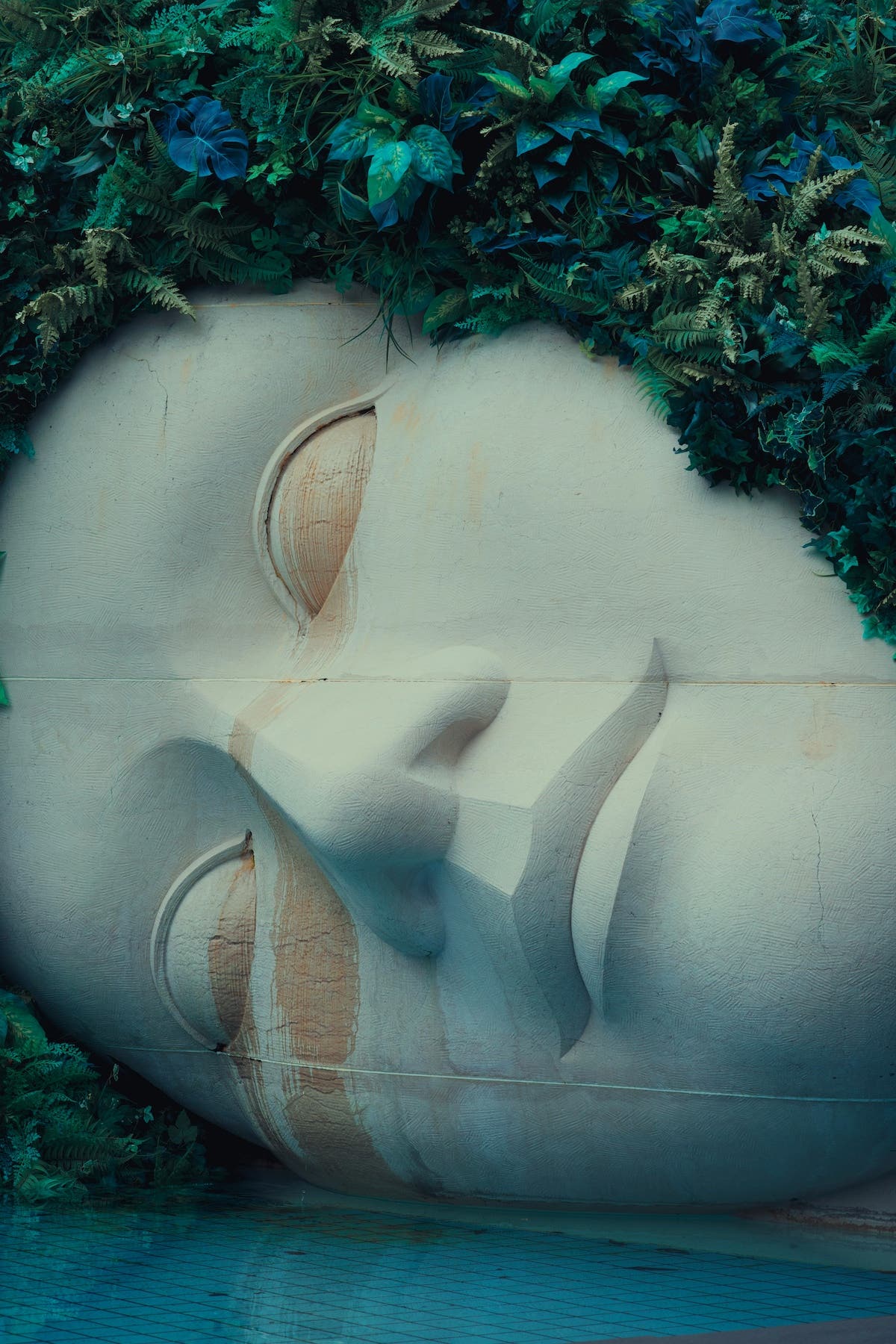 huge marble statue of a woman's face laying on its side covered in vines